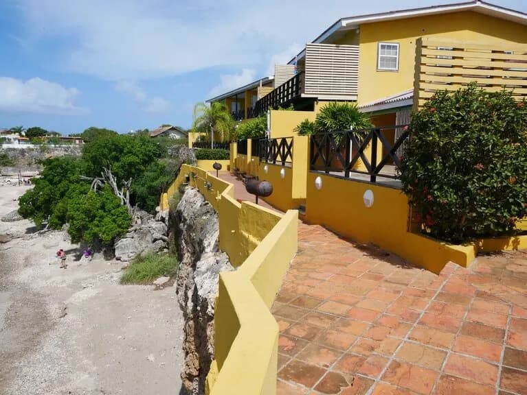 A sunny beachfront apartment with a yellow facade and a pathway leading to it.
